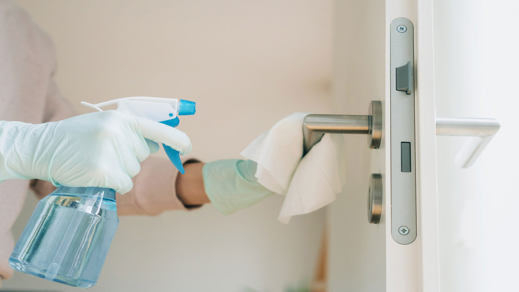 Person disinfecting a door handle with cleaner and a cloth